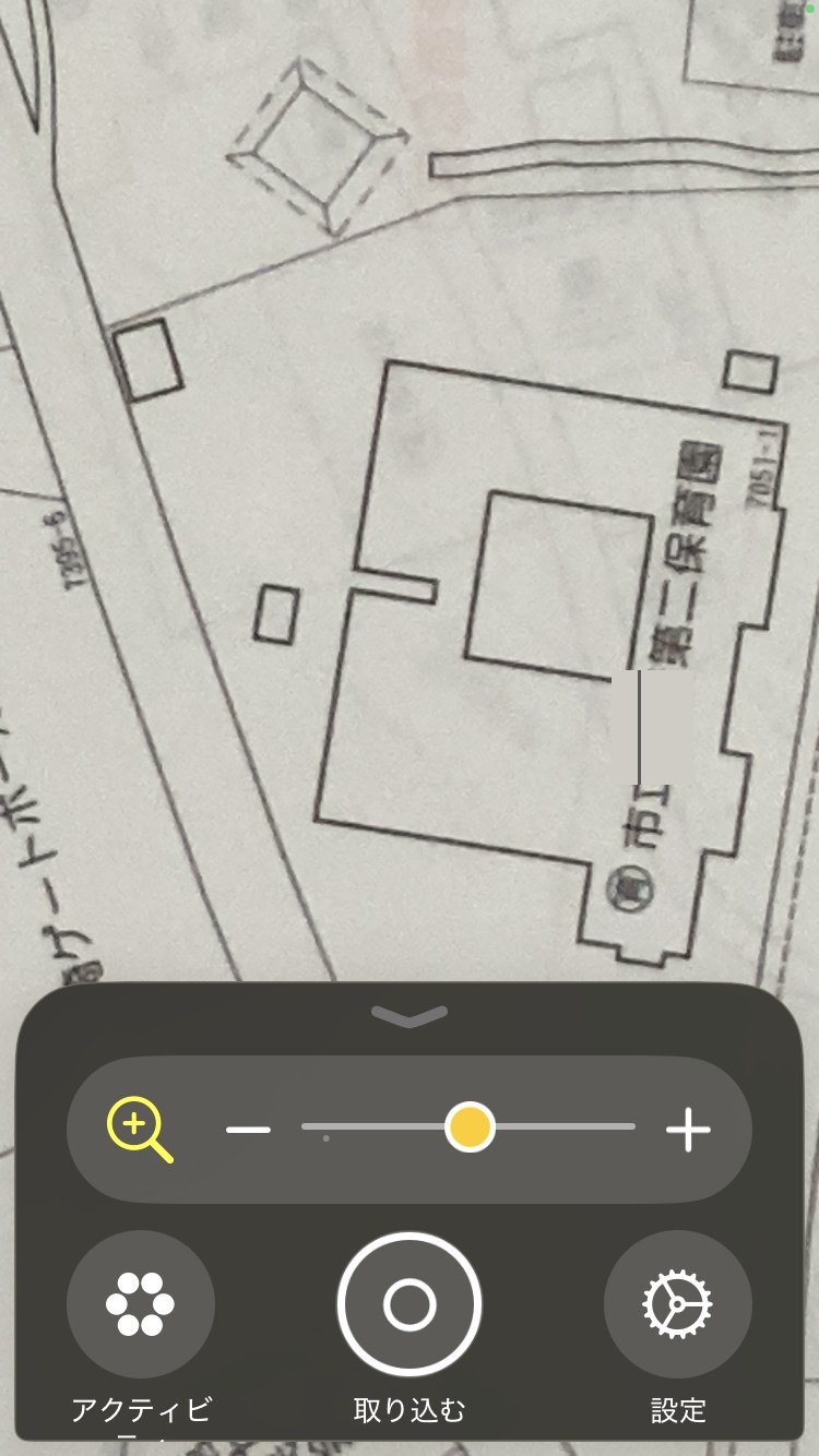 iPhoneの拡大鏡の画面。下に倍率のスライダーとプラス・マイナスのボタンが並び、住宅地図の保育園と番地が拡大されて読める